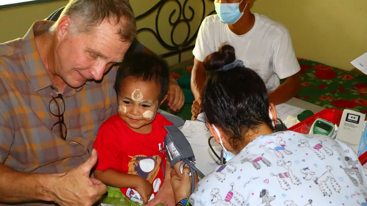 A VisionNext partner and a colleague with a smiling young boy during a community visit at a school